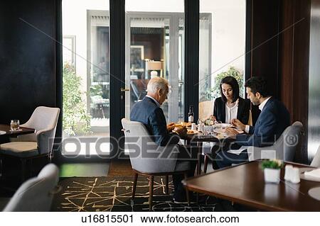 Stock Image - Two businessmen and woman having working lunch in hotel restaurant. Fotosearch