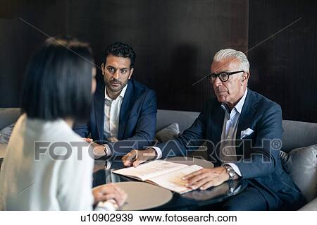 Two businessmen sitting in hotel table meeting with businesswoman View Large Photo Image Stock Photo - Two businessmen sitting in hotel table meeting with businesswoman. Fotosearch