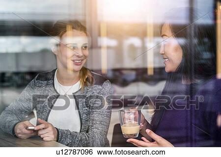 Two female students having coffee in cafe window seat View Large Photo Image Stock Photograph - Two female students having coffee in cafe window seat. Fotosearch