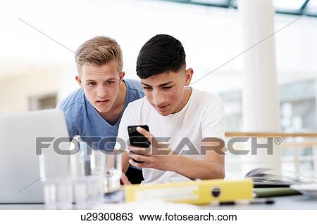 Two high school boys at classroom desk looking at smartphone View Large Photo Image Stock Image - Two high school boys at classroom desk looking at smartphone. Fotosearch