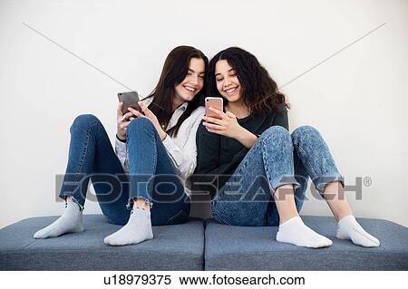 Stock Photography - Two high school girls on seating looking at smartphones. Fotosearch