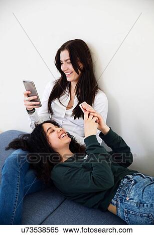 Stock Photography - Two high school girls on seating looking at smartphones. Fotosearch