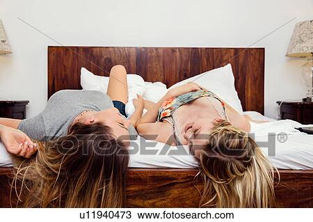 Stock Image - Two women lying on bed chatting. Fotosearch