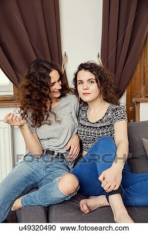 Stock Image - Two young female friends sitting on sofa portrait. Fotosearch