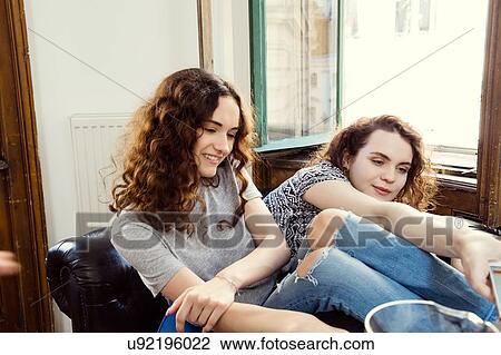 Stock Image - Two young female friends sitting on armchair. Fotosearch