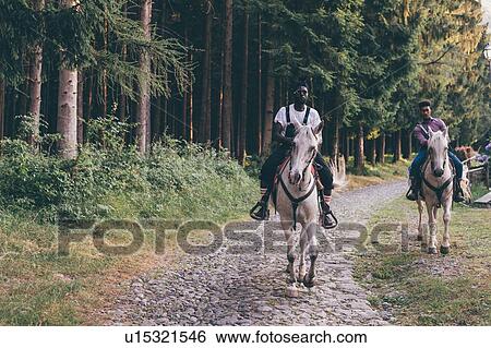 Stock Photograph - Two young men riding horses on rural cobbled road, Primaluna, Trentino-Alto Adige, Italy. Fotosearch