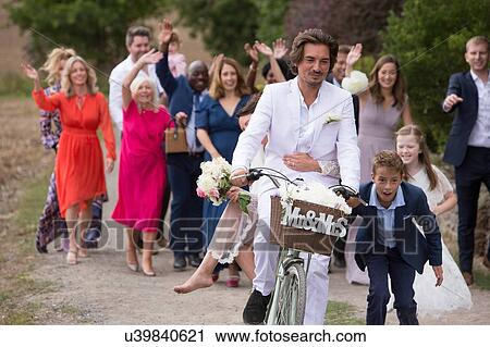 Stock Image - Wedding guests waving off newlyweds on bicycles. Fotosearch