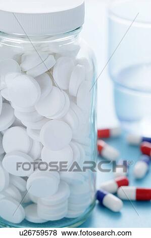 Stock Photo - White pills in a glass bottle and a glass of water with various other drug capsules in the background.. Fotosearch