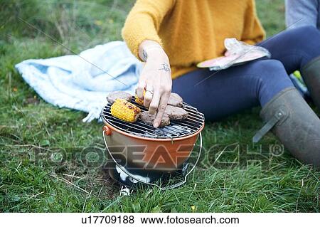 Stock Photo - Woman and boyfriend sitting in rural field cooking on barbecue grill, cropped. Fotosearch