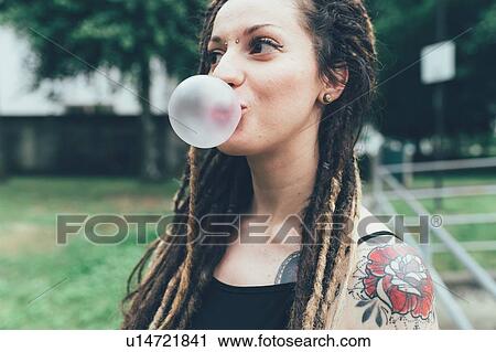 Stock Image - Woman blowing bubble gum in park. Fotosearch