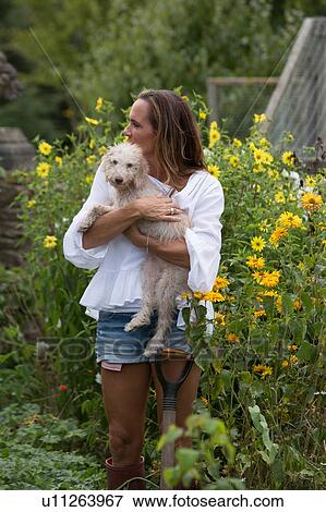 Stock Photo - Woman carrying pet dog in garden. Fotosearch