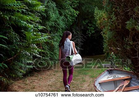 Stock Image - Woman carrying yoga mat strolling through garden. Fotosearch