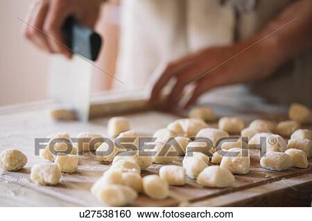 Stock Image - Woman cutting dough for gnocchi. Fotosearch