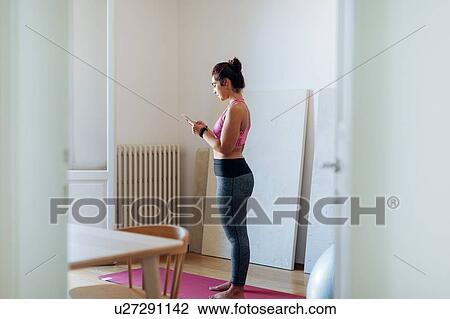 Stock Image - Woman doing exercise and texting at home. Fotosearch