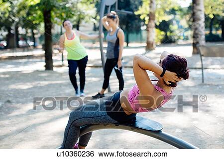 Woman doing sit ups in park, friends in background View Large Photo Image Stock Photograph - Woman doing sit ups in park, friends in background. Fotosearch