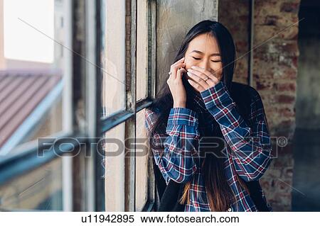 Stock Photography - Woman giggling on smartphone with hand over mouth. Fotosearch