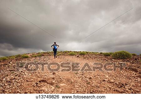 Stock Photograph - Woman hiking up hill on dirt track, rear view, Las Palmas, Gran Canaria, Canary Islands, Spain. Fotosearch