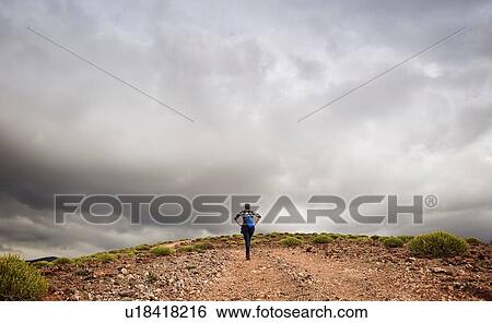 Stock Photograph - Woman hiking up hill on dirt track, rear view, Las Palmas, Gran Canaria, Canary Islands, Spain. Fotosearch