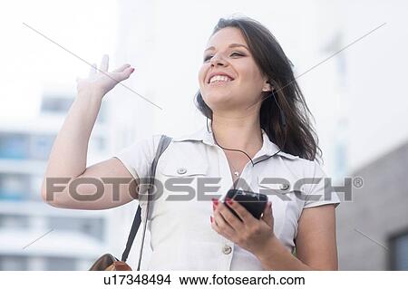Picture - Woman holding smartphone and waving. Fotosearch