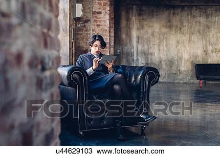Woman in armchair using digital tablet View Large Photo Image Stock Image - Woman in armchair using digital tablet. Fotosearch