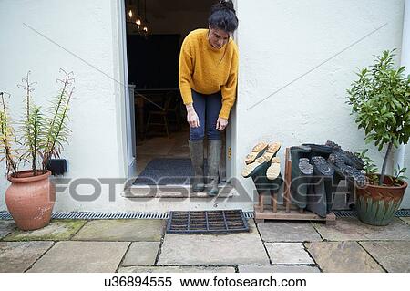 Stock Photography - Woman in doorway beside wellies. Fotosearch