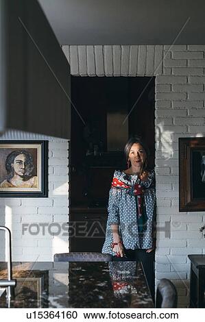Stock Image - Woman leaning against doorway of kitchen. Fotosearch