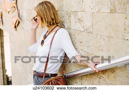 Stock Image - Woman leaning against stone wall. Fotosearch