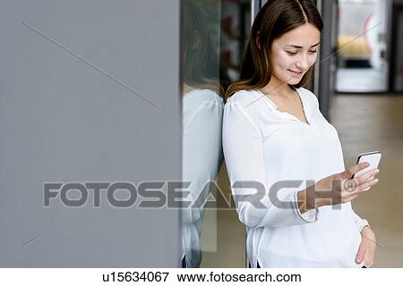 Stock Photo - Woman leaning on glass wall using cellphone. Fotosearch