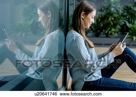 Stock Photograph - Woman leaning on glass wall using digital tablet. Fotosearch