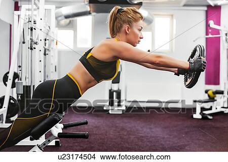 Picture - Woman lifting weight disc and leaning forward in gym. Fotosearch