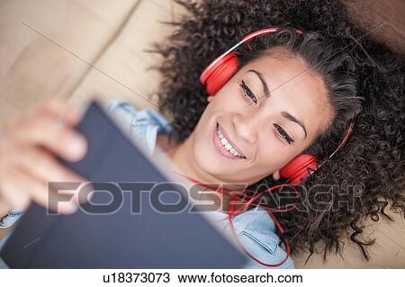 Stock Image - Woman listening to music on digital tablet at home. Fotosearch