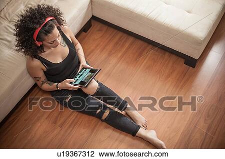 Stock Image - Woman listening to music on digital tablet at home. Fotosearch