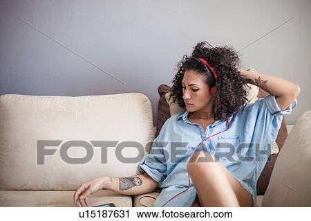 Stock Image - Woman listening to music on mobile phone at home. Fotosearch
