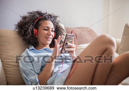 Stock Photo - Woman listening to music on mobile phone at home. Fotosearch