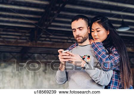 Woman looking over shoulder of man using smartphone View Large Photo Image Stock Photo - Woman looking over shoulder of man using smartphone. Fotosearch