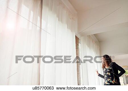Woman peering out through net curtained window View Large Photo Image Stock Image - Woman peering out through net curtained window. Fotosearch