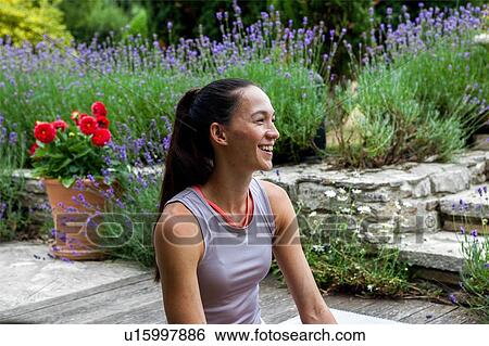 Stock Photograph - Woman practicing yoga in garden, taking a break on patio. Fotosearch