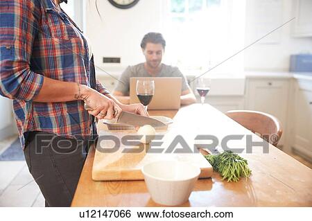 Woman preparing vegetables at kitchen table, boyfriend using laptop View Large Photo Image Stock Photograph - Woman preparing vegetables at kitchen table, boyfriend using laptop. Fotosearch