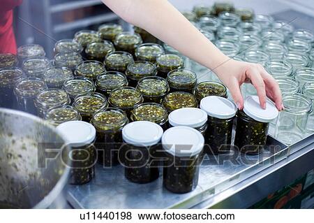 Stock Photo - Woman putting lids on jars of jam in industrial kitchen, close up of hand. Fotosearch