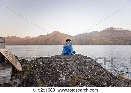 Stock Photo - Woman relaxing by lakeside, Johnstone Strait, Telegraph Cove, Canada. Fotosearch