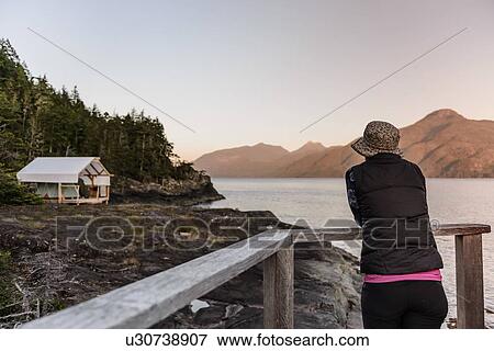 Stock Photo - Woman relaxing by lakeside, Johnstone Strait, Telegraph Cove, Canada. Fotosearch