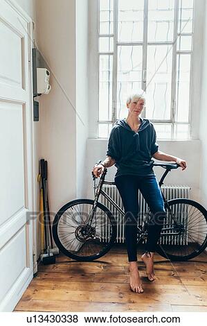 Stock Photo - Woman sitting on bicycle at home. Fotosearch