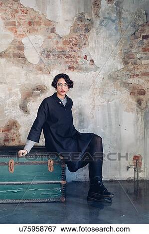 Stock Photo - Woman sitting on box, concrete wall in background. Fotosearch