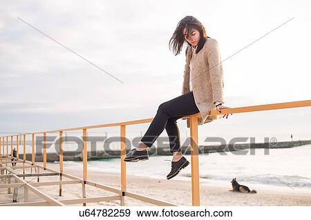 Woman sitting on handrail at beach View Large Photo Image Stock Photo - Woman sitting on handrail at beach. Fotosearch