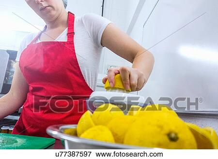 Stock Photo - Woman squeezing fresh lemons for jam making in industrial kitchen, mid section. Fotosearch
