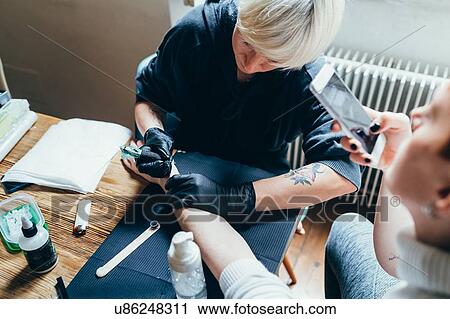 Woman tattooing friend's arm at home View Large Photo Image Stock Image - Woman tattooing friend's arm at home. Fotosearch