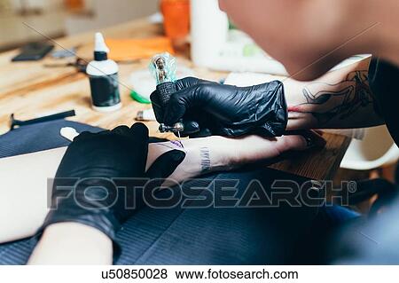 Stock Photo - Woman tattooing friend's arm at home. Fotosearch