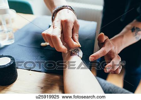 Stock Photography - Woman tattooing friend's arm at home. Fotosearch