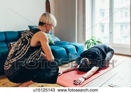 Stock Image - Woman teaching friend yoga at home. Fotosearch