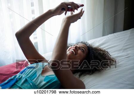 Stock Photo - Woman texting on bed. Fotosearch